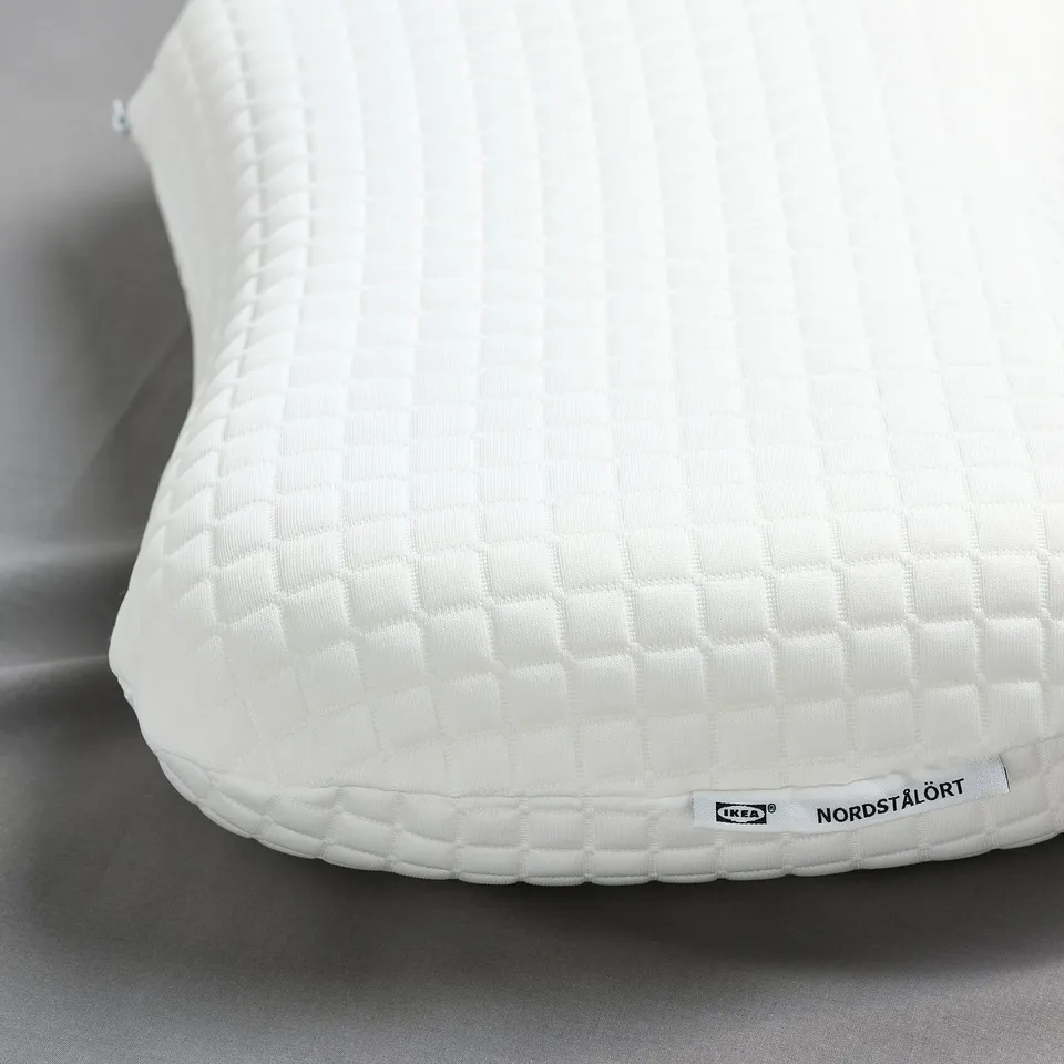 Close-up of a white ergonomic pillow by IKEA, showcasing its textured, quilted surface, featuring the NORDSTÅLÖRT branding.