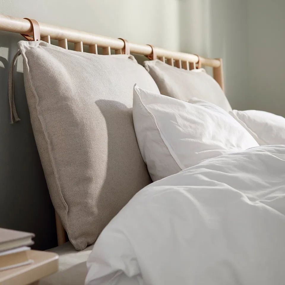 White bed with wooden headboard, three pillows, light blanket, and small books on bedside. Calm, minimalist decor.