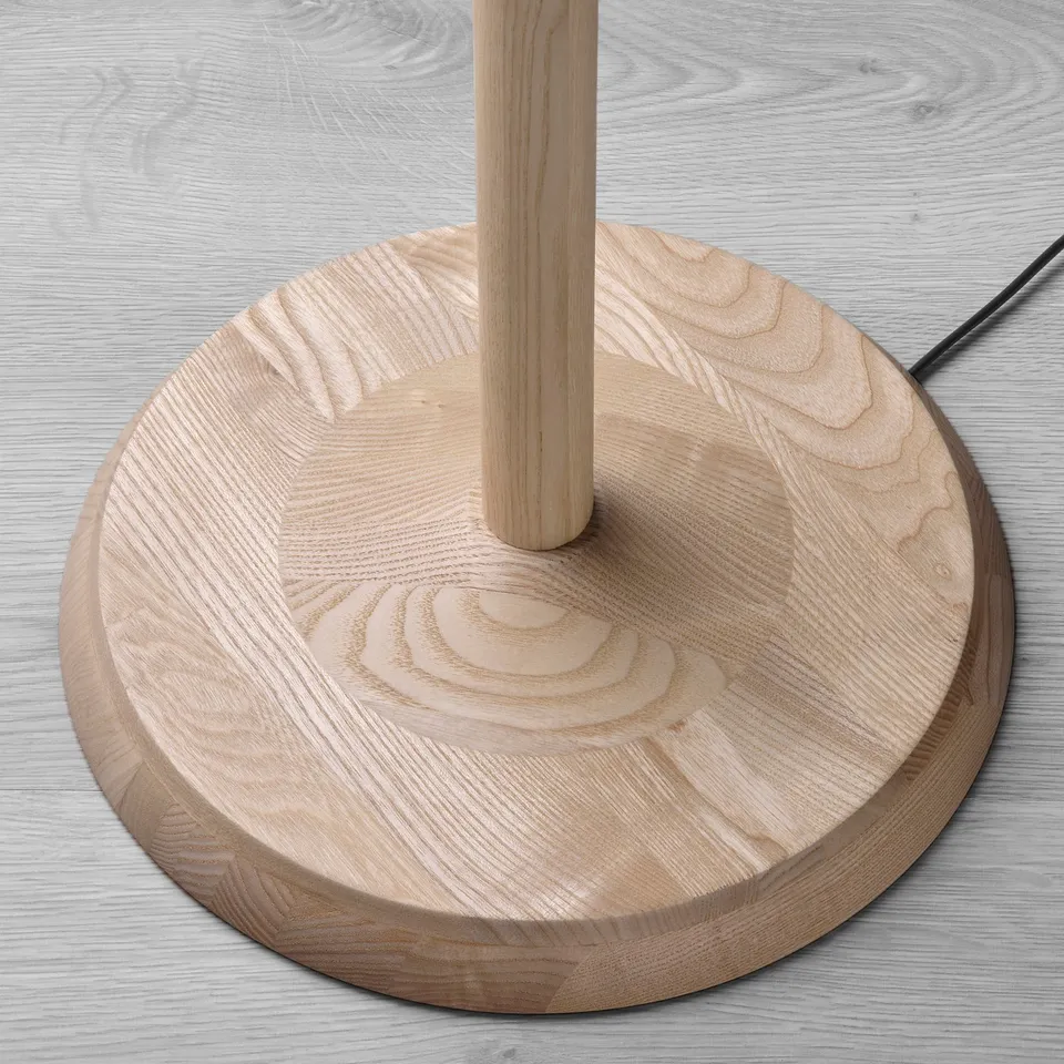 Round wooden base for floor lamp. Crafted from solid ash, showcasing natural grain. Central support holds main structure.