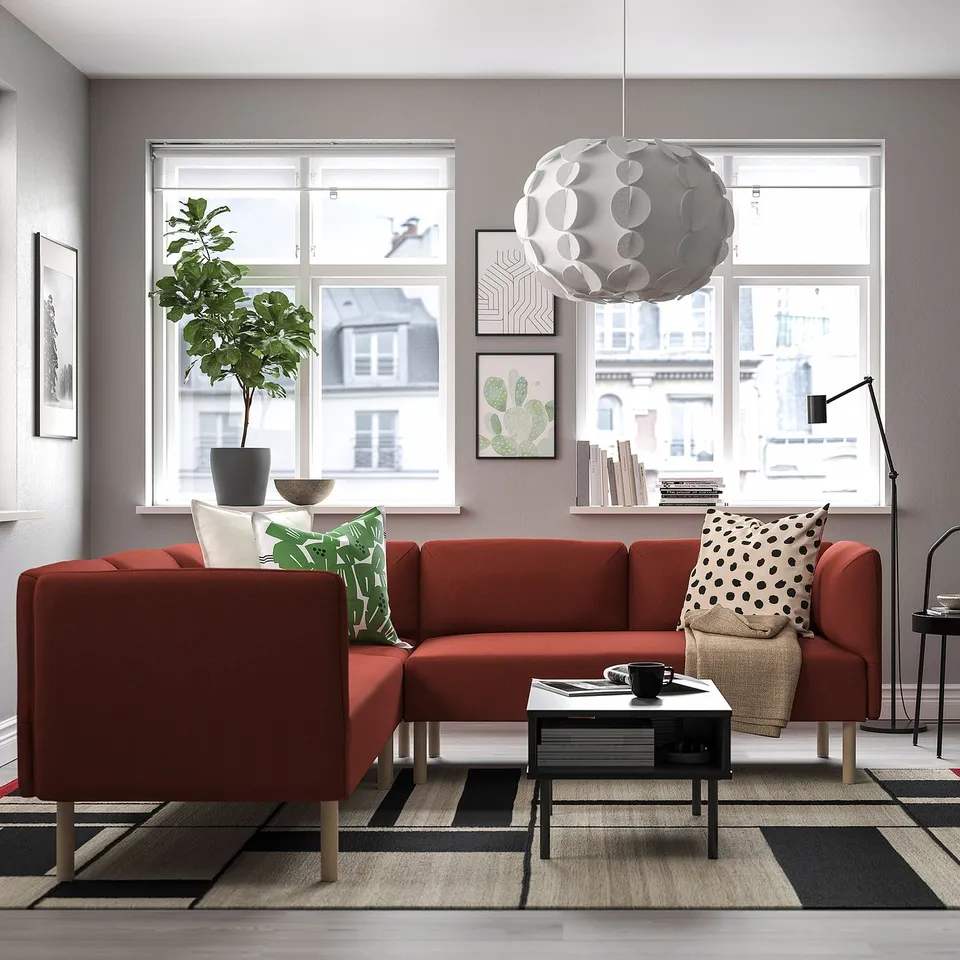 Modern living room with red sofa, rug, city view, vibrant decor.