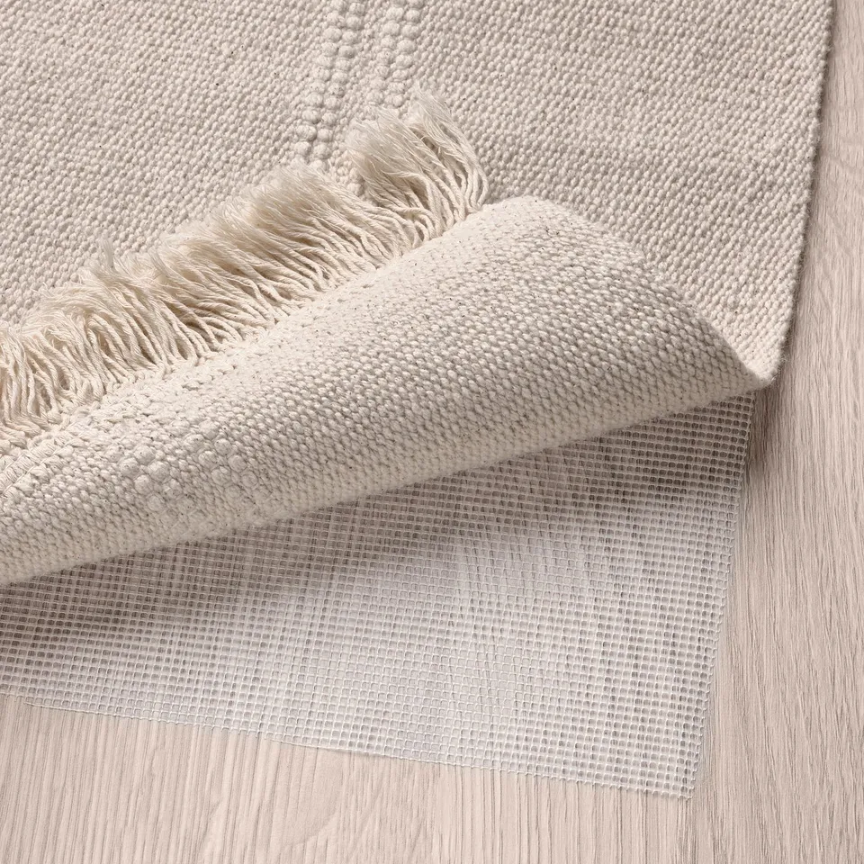 Beige rug with fringed edge & mesh underlay.