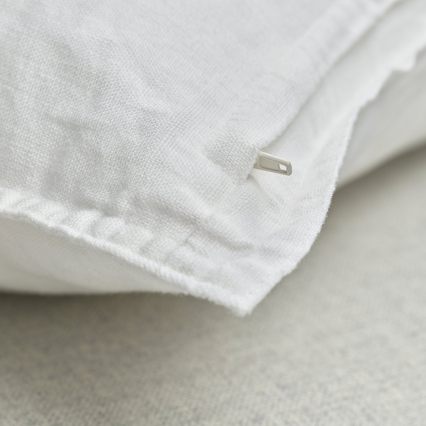 Close-up of white linen cushion cover with hidden zip, showcasing soft, textured fabric.