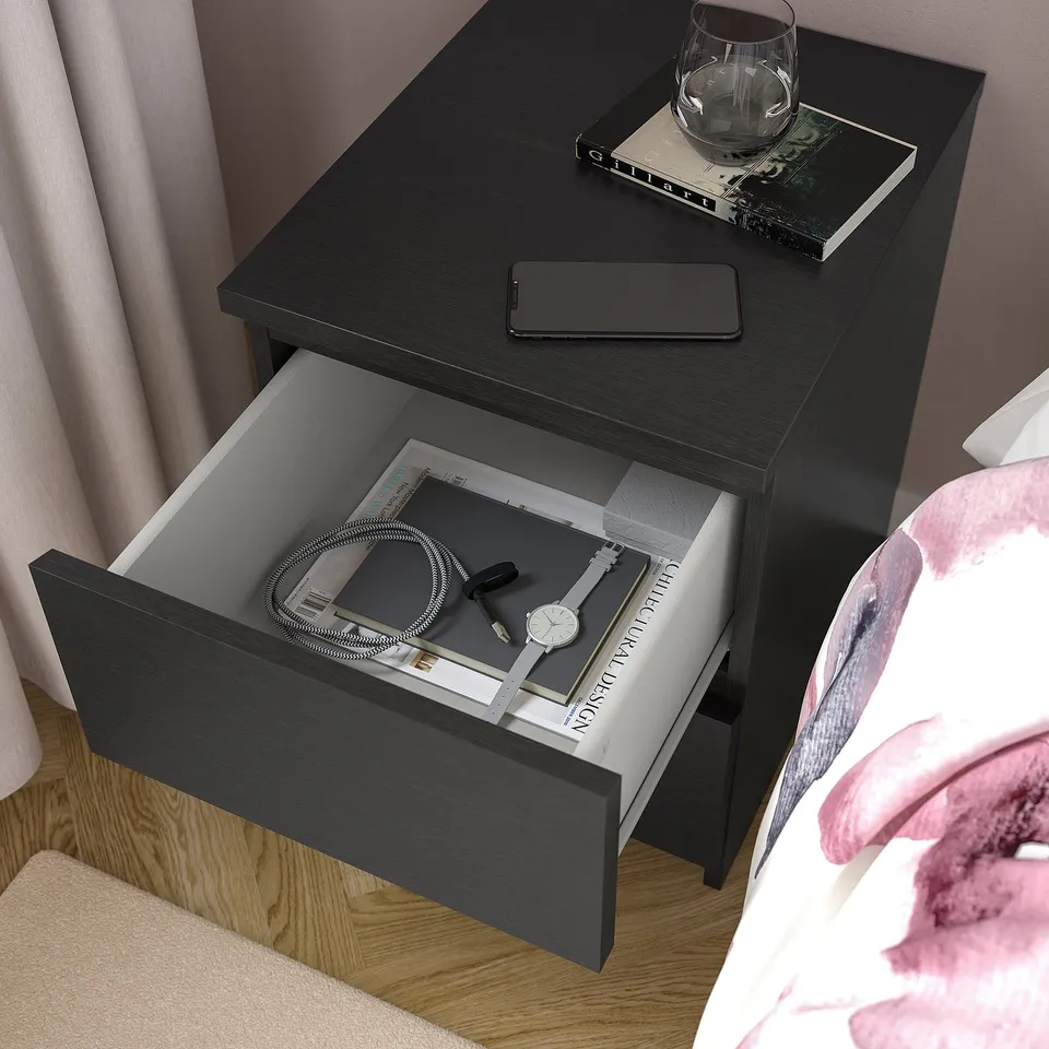 Black bedside table with an open drawer showing a watch and charger.