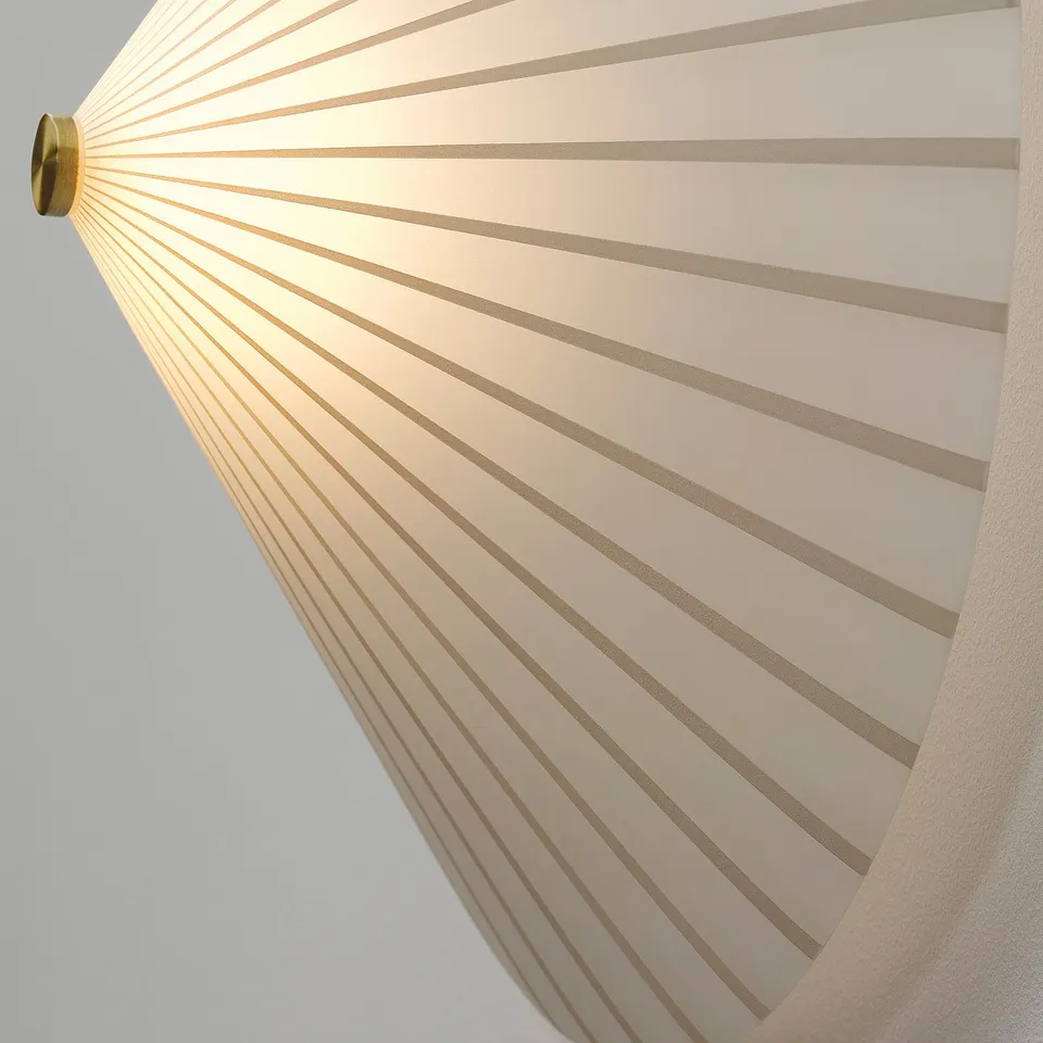 A modern wall lamp with a striped, opaque glass shade casting soft, diffused light. Gold-colored metal fixture.