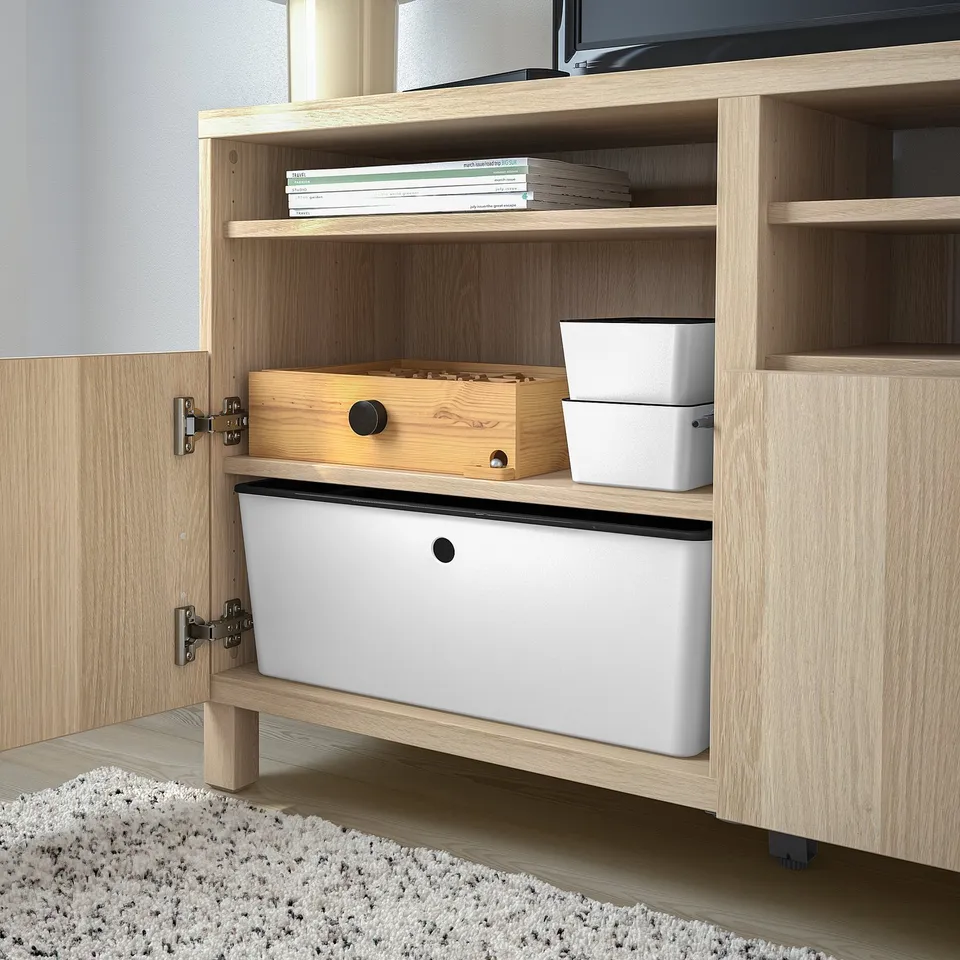 Wooden cabinet open showing storage: white bins, wooden box, stacked books. Ideal for organising games, arts, or hobbies.