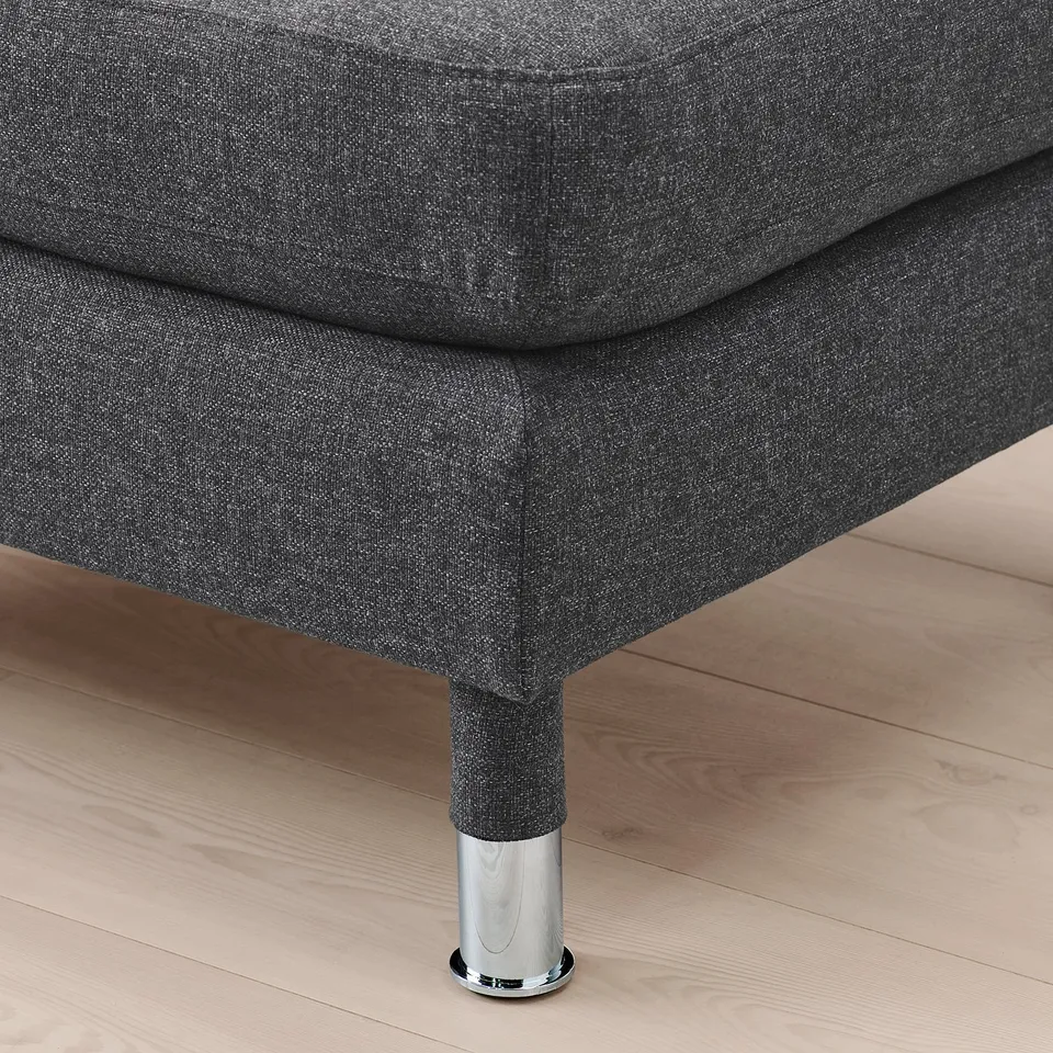 Close-up of a stylish footstool with dark grey upholstery and chrome leg on a wooden floor.
