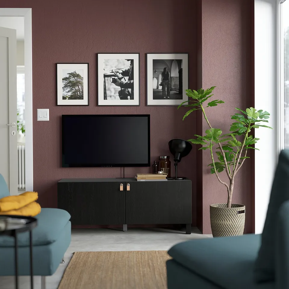 Modern living room with maroon walls, BESTÅ tv stand, blue armchairs, and plant.