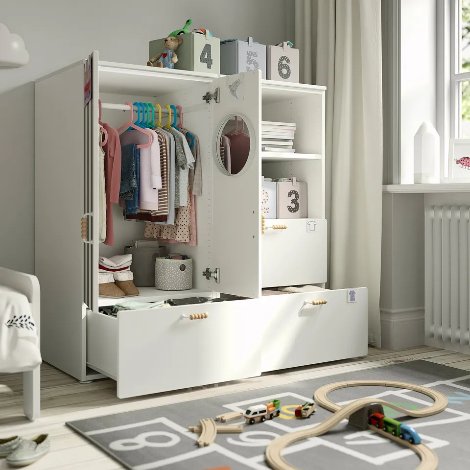 Childs room with white wardrobe, clothes, toys, and mirror.