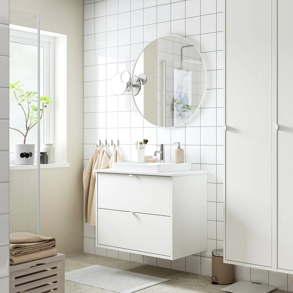 Modern white bathroom setup with wall-mounted HAVBÄCK vanity, round mirror, and small towels.