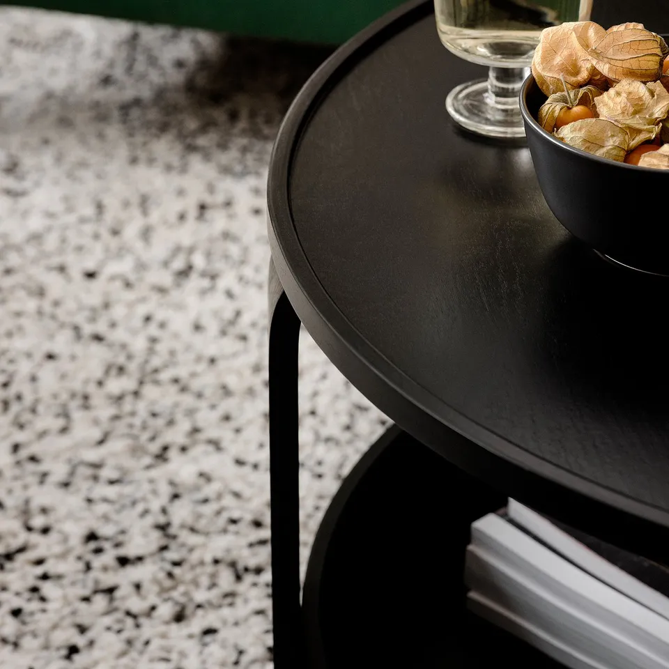 Black circular BORGEBY storage table with dried plants and a glass, exhibiting its organised and stylish design.