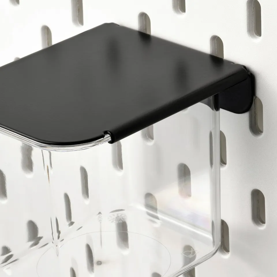 Clear plastic storage container with dark grey lid attached to a white pegboard. High-quality, durable design for organised storage.