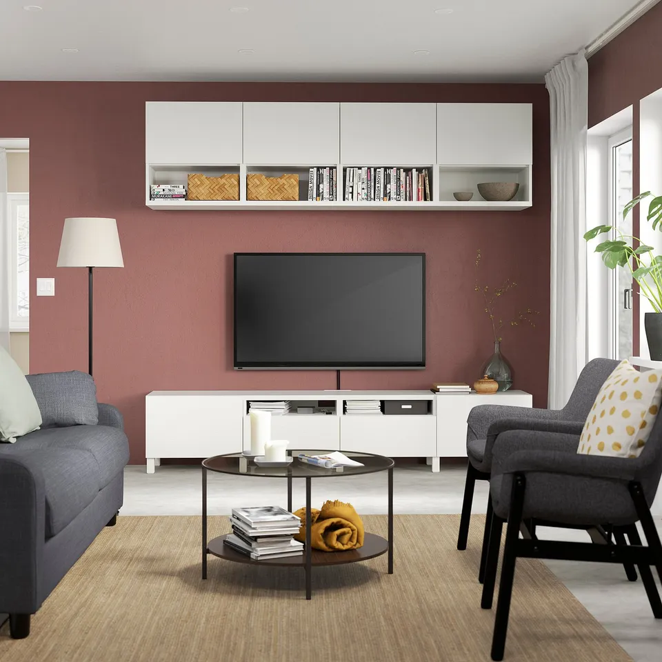 Modern living room with red walls, grey sofa and chair, white tv unit, black coffee table with books and blanket, and adjustable wooden legs.