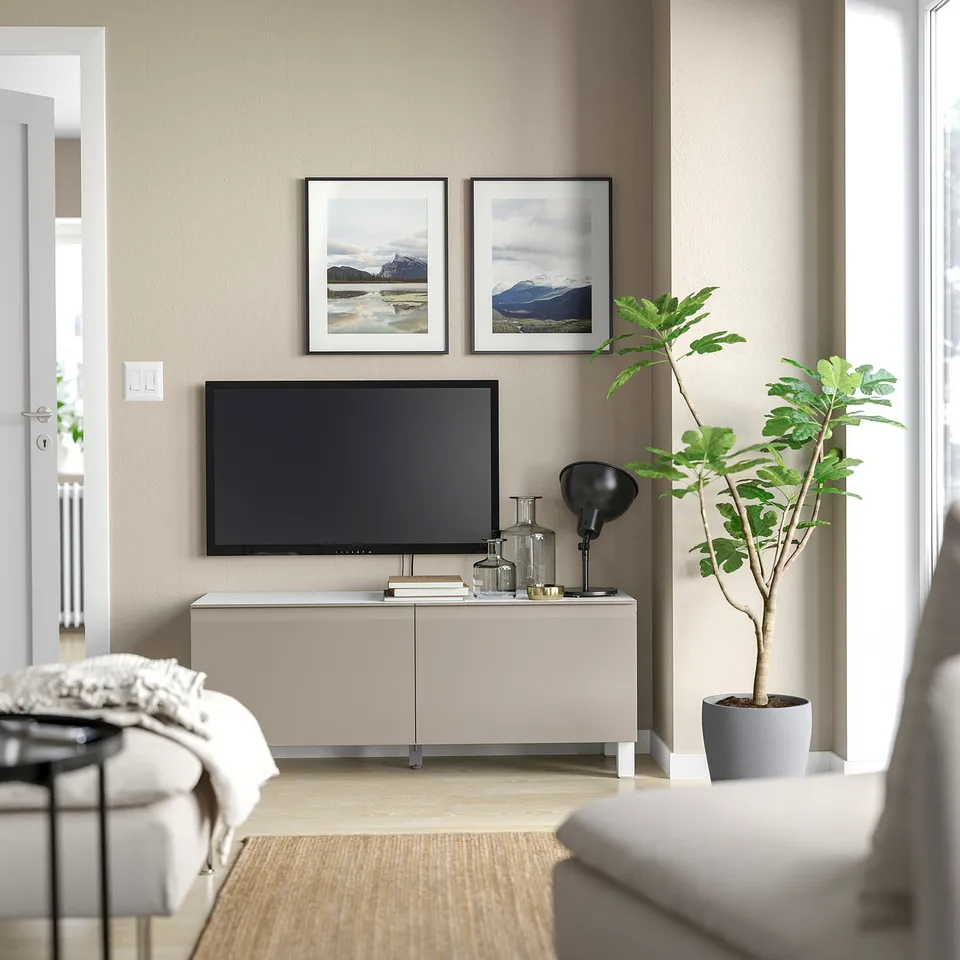 Modern living room with beige BESTÅ tv stand, flat screen tv, potted plant, and framed nature photos.