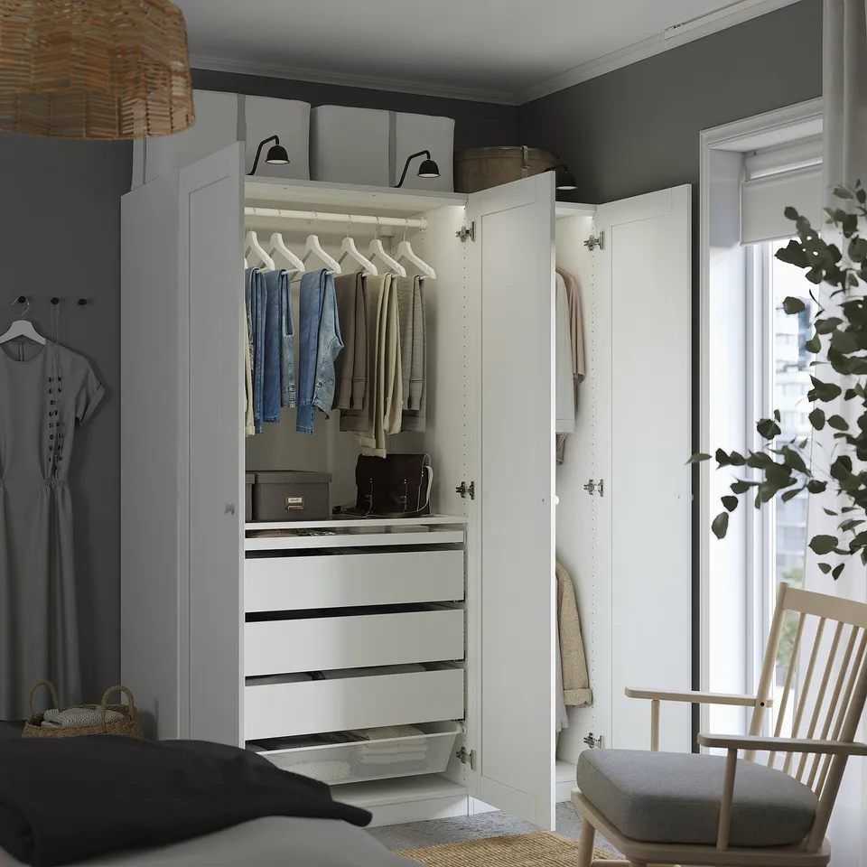 Modern bedroom with open PAX wardrobe displaying clothes, accessories, and storage solutions.