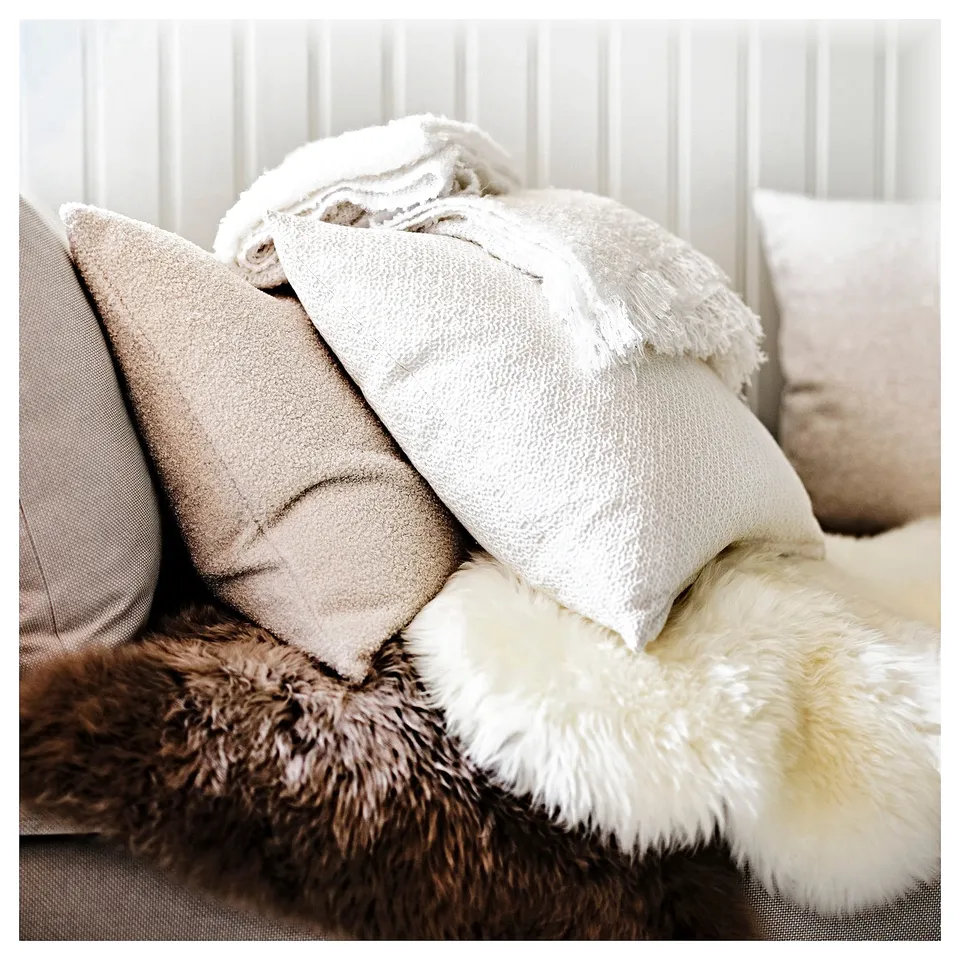Beige ULLERSLEV sheepskin rug on light couch/floor, cosy and soft.