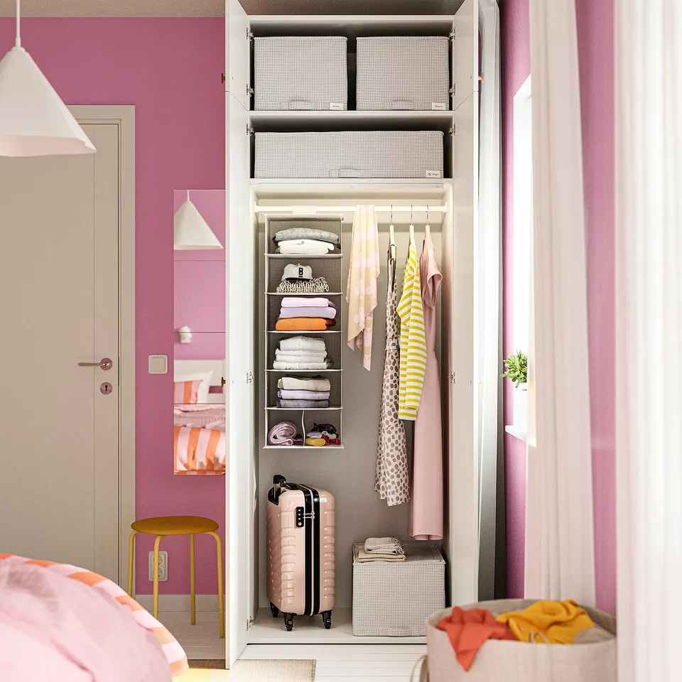 Closet with pink walls, white hanging clothes organiser, shelves, suitcase, and folded shirts.