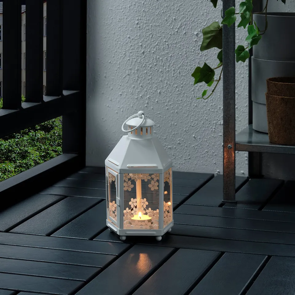 White KRINGSYNT lantern on deck, lit candle inside, casts warm glow, sits upright.