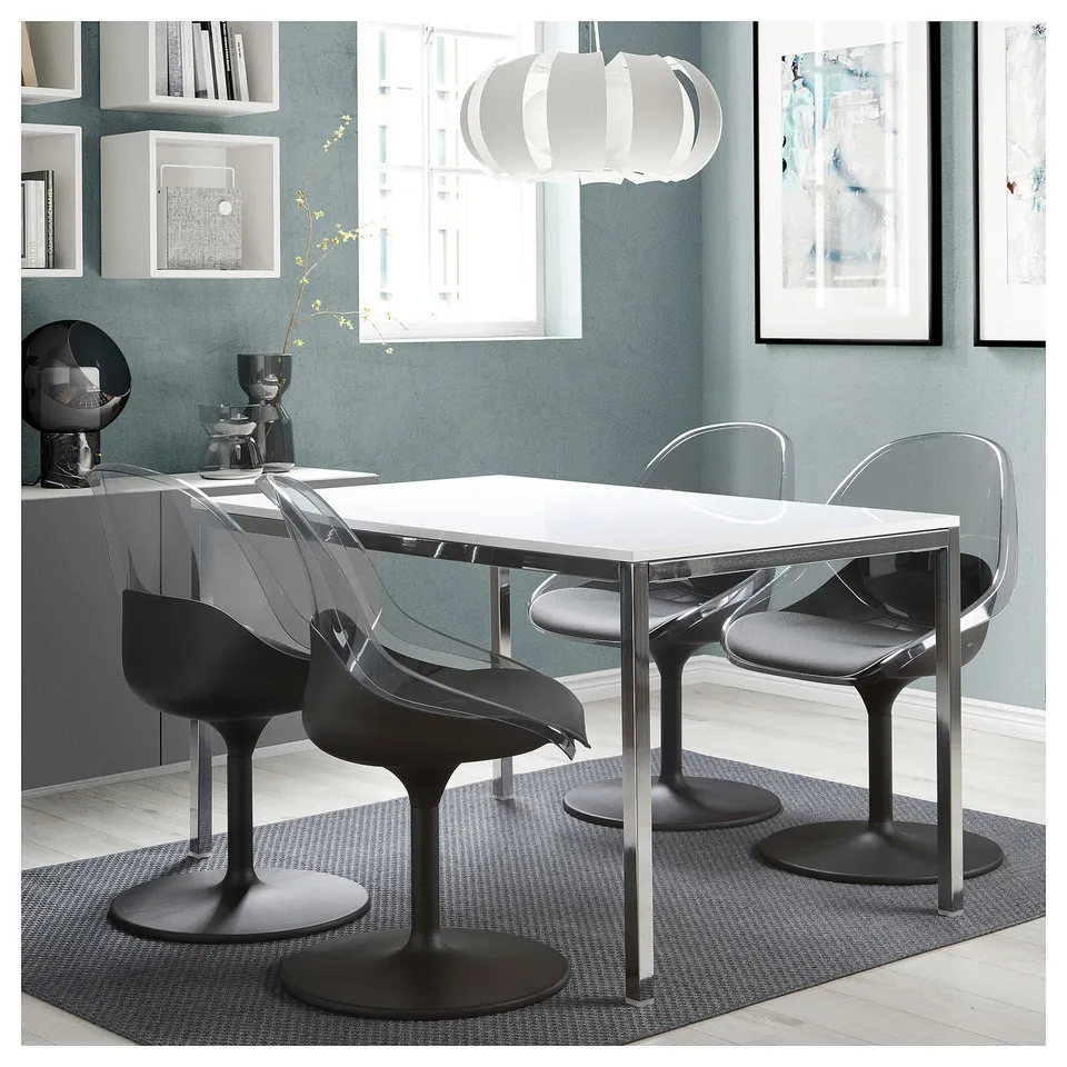Modern dining area with BALTSAR black swivel chairs, clear back, glass table, blue rug, blue wall, white pendant light, and grey artwork.