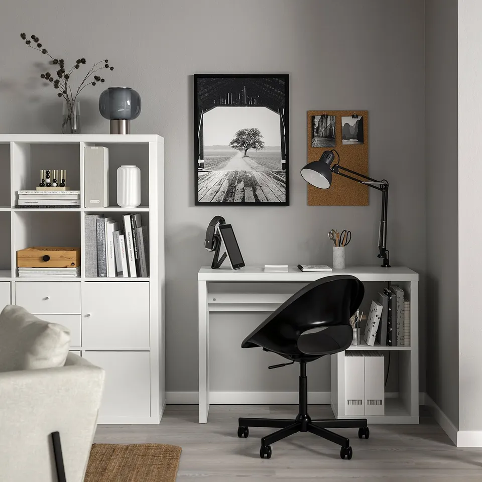 Home office with KALLAX shelf, black chair, desk organised with lamp, tablet, books. Wall has artwork and cork board.