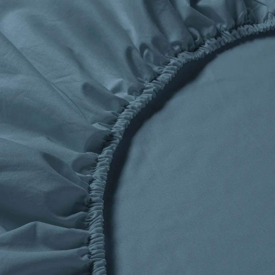 Blue bed sheet with gathered, elastic edges, laid flat on a surface.