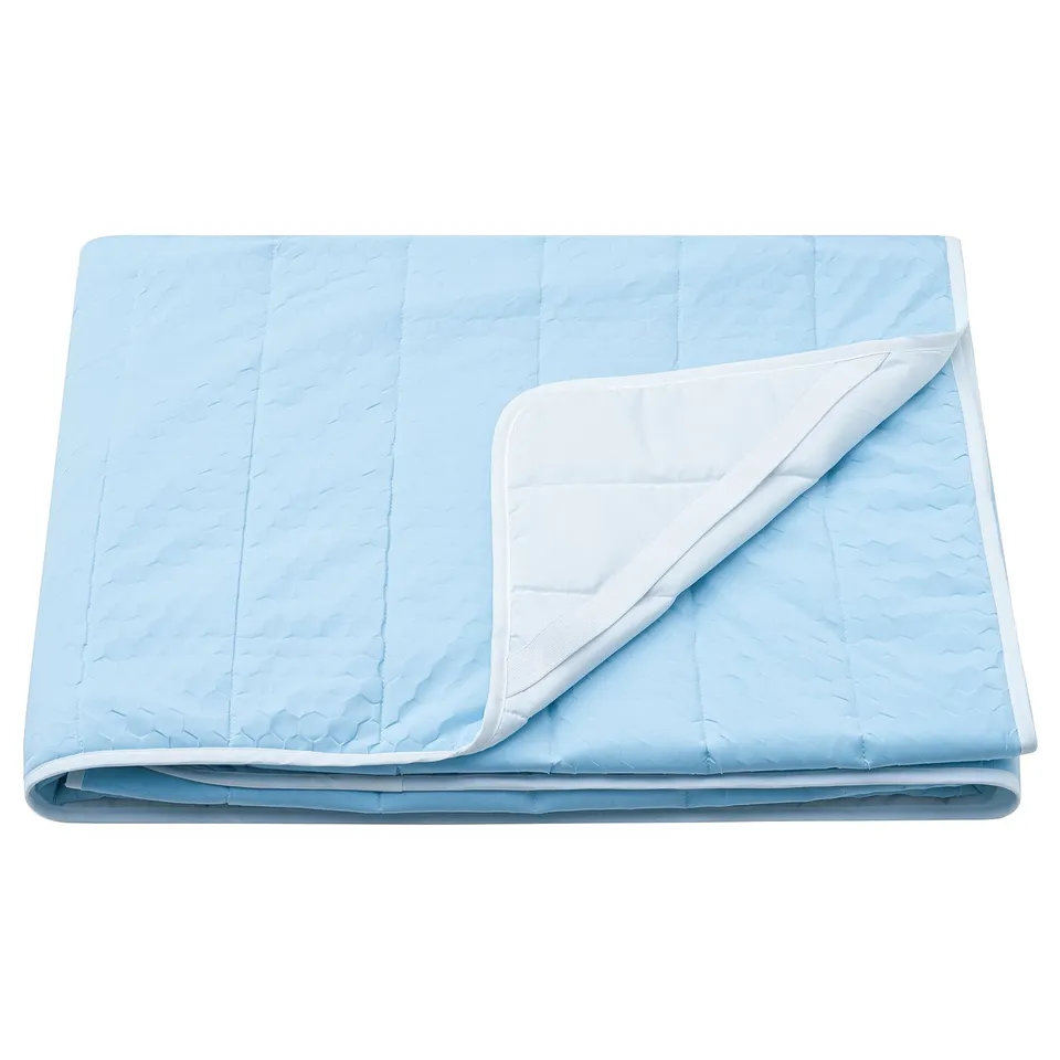 Displays a light blue, folded mattress protector with a white edge, featuring a textured diamond pattern and recycled materials.