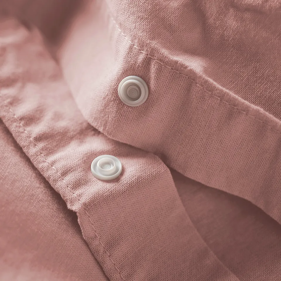 Close-up of soft pink duvet with two white buttons. Buttons fasten the fabric, ensuring the cover stays in place.