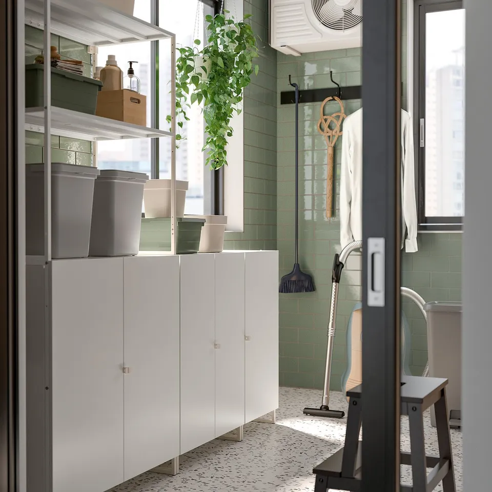 Well-organized utility room with white JOSTEIN storage cabinets, grey containers, hanging tools, and a green indoor plant.