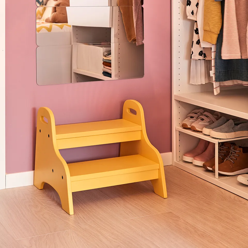 Small kids yellow stool in room with pink walls, clothes, and mirror.