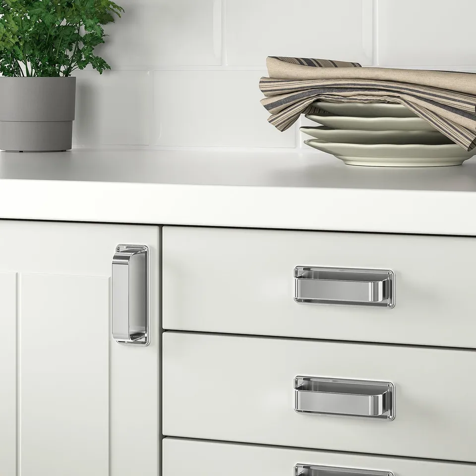 White kitchen cabinets with chrome SÖRBYN handles, stack of plates and towels on countertop.