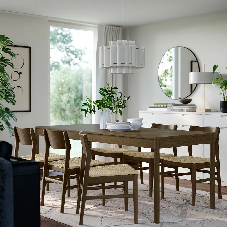 Modern dining set with wooden table, wicker chairs, sleek chandelier, and white decor.