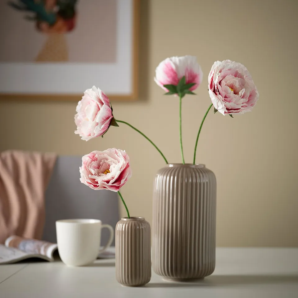 Beige stoneware vase with grooves holding pink flowers, alongside white mug and smaller vase.