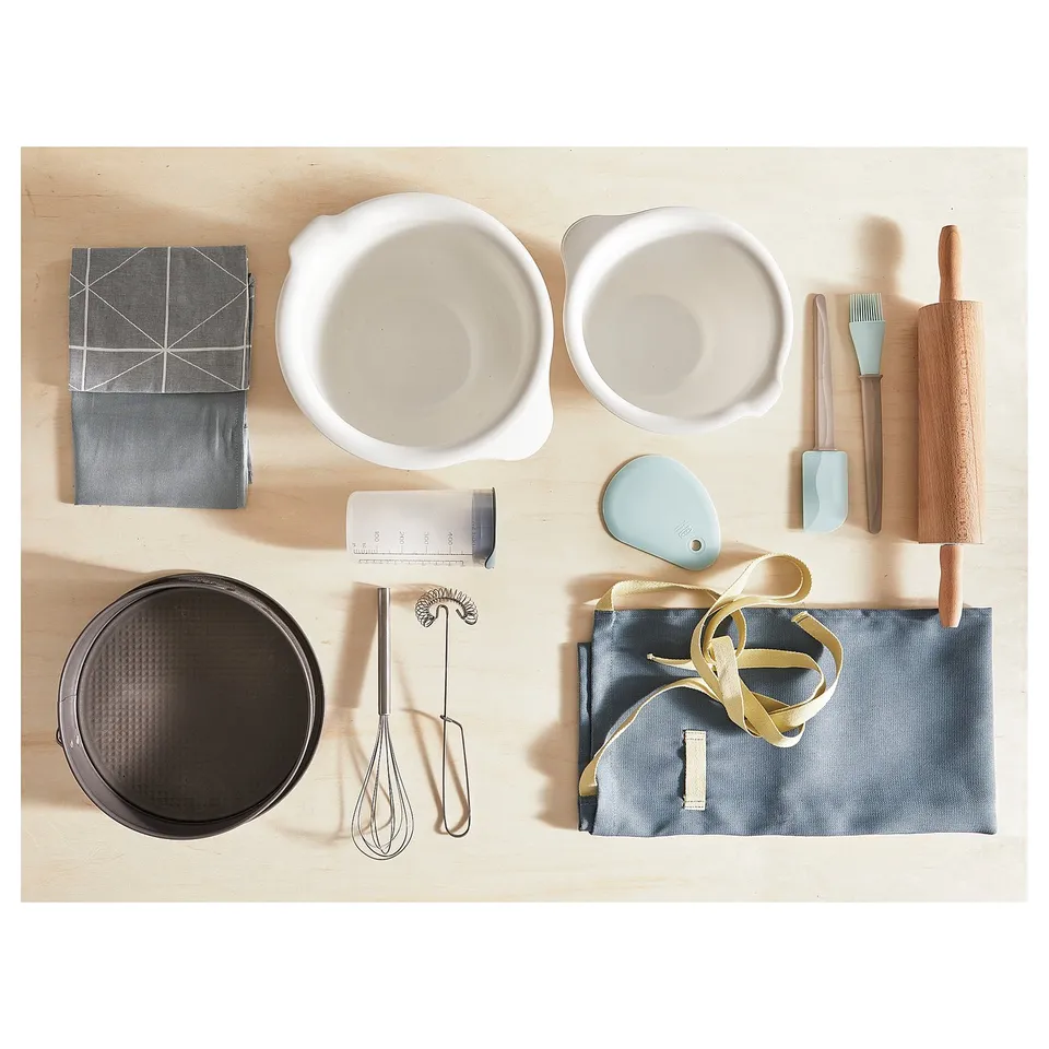 Baking tools: bowls, towels, utensils, scraper, ribbon, sieve, whisk, measurer, beige background.