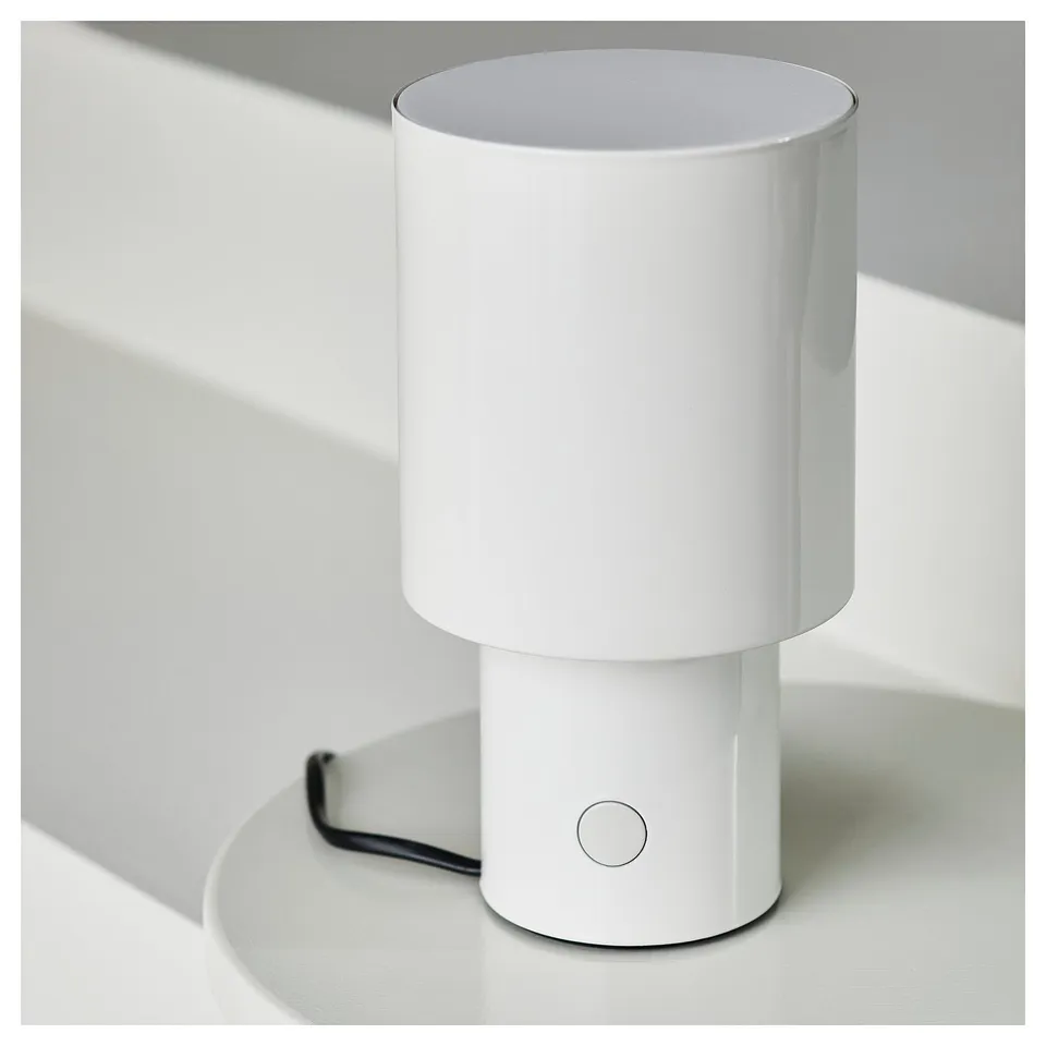 Small white table lamp on a white surface with a sleek design, emitting a balanced, soft light upwards and downwards.