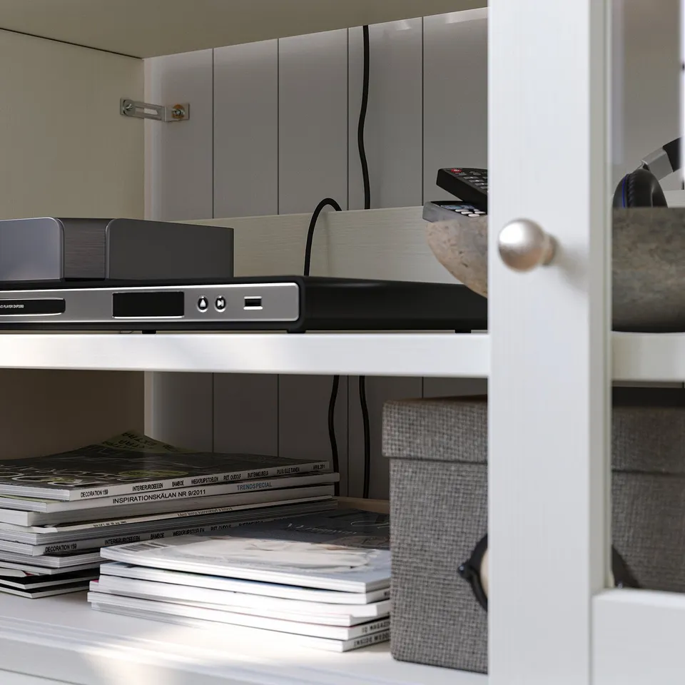 White wooden tv unit with shelves, storing magazines, a dvd player, and remotes. Black and silver electronics contrast with light shelves.
