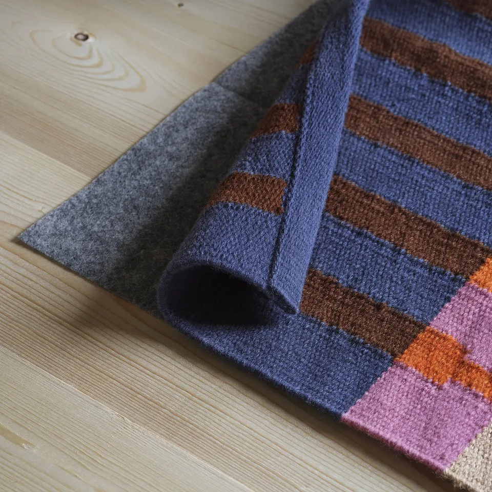 Folded striped rug in blues, browns, and pinks on wooden floor. It is flat, durable, and ideal for hallways.