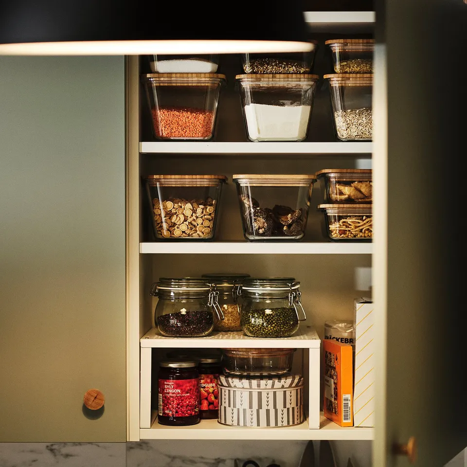 An open cabinet with KORKEN jars storing various dry goods, pickles, and jams. Jars sealed for airtight preservation.