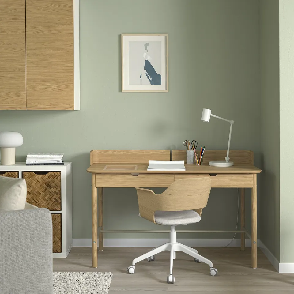 Home office: light wood desk & grey chair, green wall, art, lamp, books.