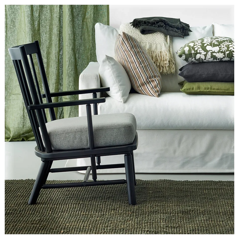 Green rug, black chair, grey cushion, white sofa with pillows, green curtains.