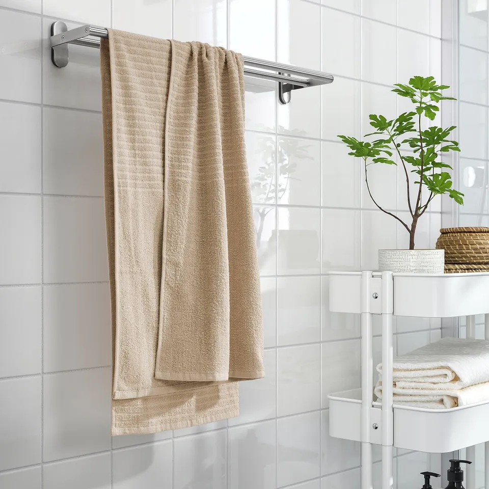 Bathroom with VÅGSJÖN towels on chrome rail, plus folded towels and plant on rack.