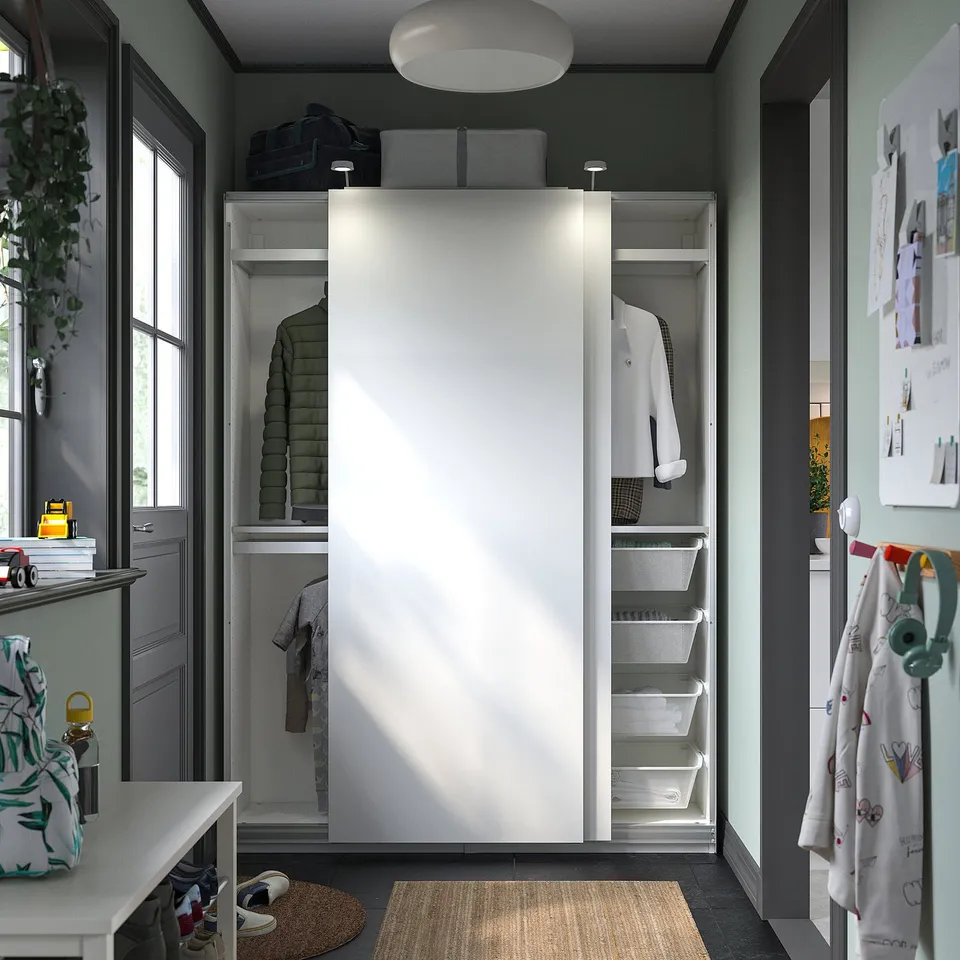 Closed white PAX wardrobe in room, with clothes inside.