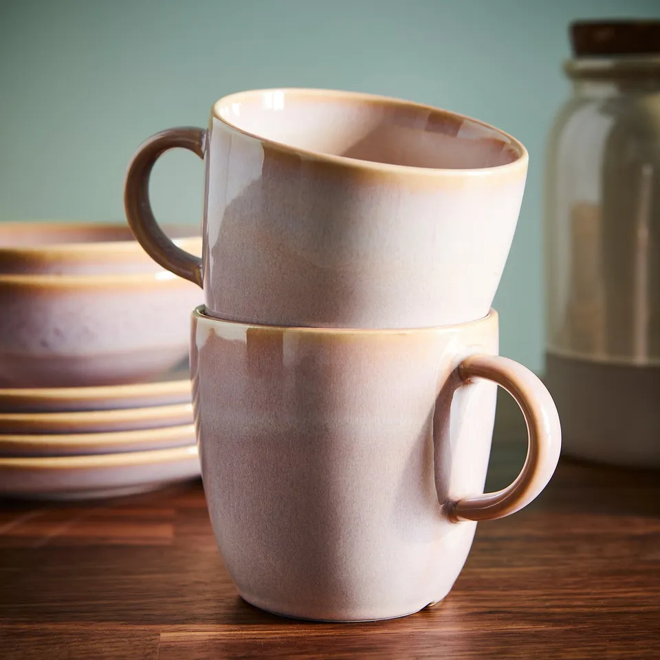 Two glazed mugs stacked on a wooden table, showcasing a rustic surface and practical design for serving coffee or tea.