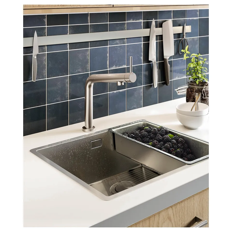 Modern kitchen sink with stainless steel tap and grey tiled backsplash, holding a colander with blackberries.