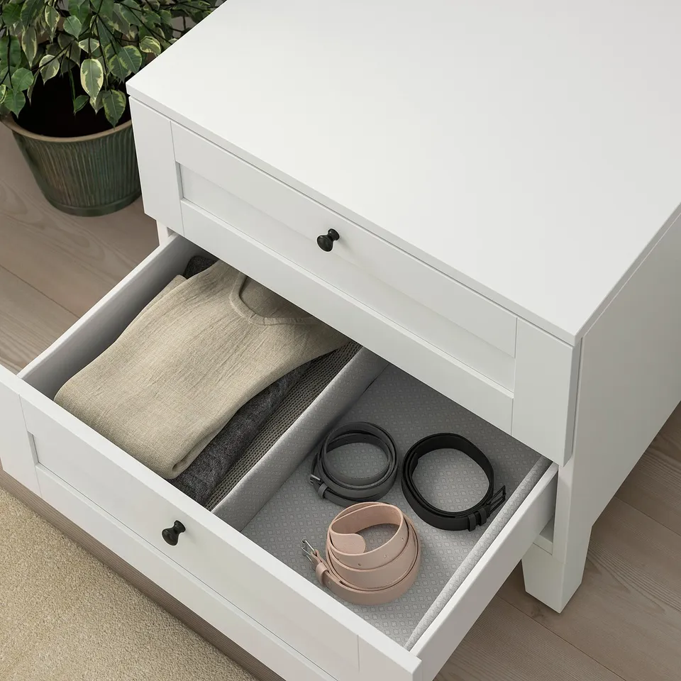 Open white PLATSA drawer showing neatly folded clothes and belts inside.