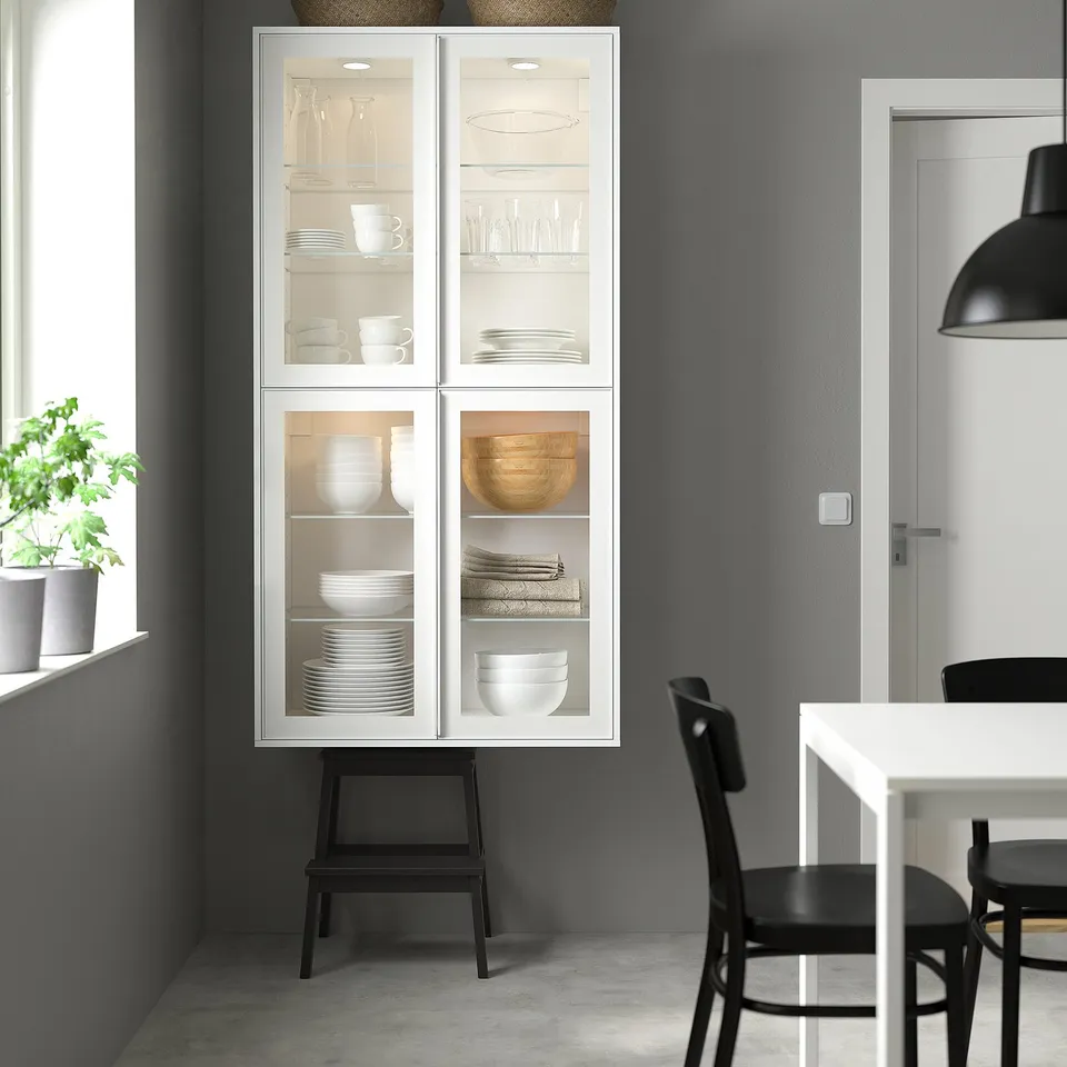 Modern kitchen with white glass-door cabinet displaying dishes, larger than the nearby dining table with black chairs.