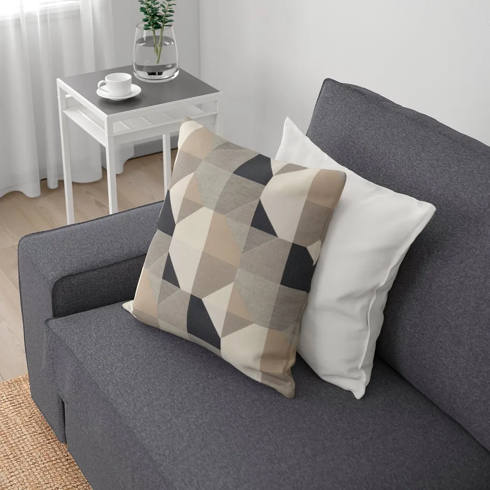 A grey KIVIK sofa with a chequered and white pillow. Its designed for comfort and relaxation.