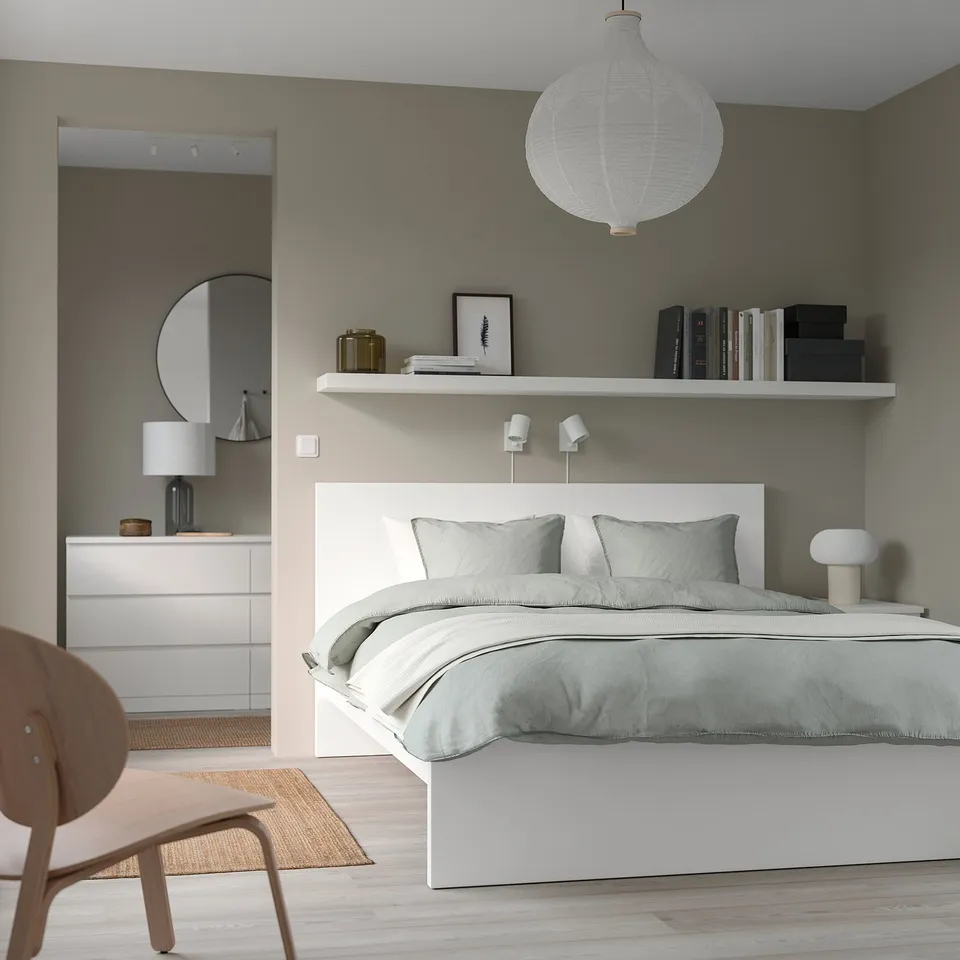 Cosy bedroom featuring MALM bed with grey linens, white shelves, and wooden chair, accented by a large pendant light.