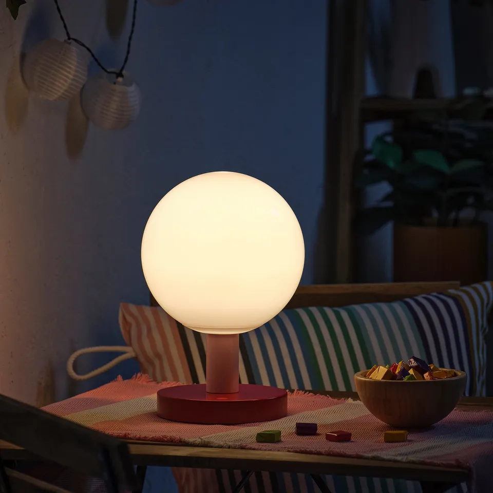 Cosy indoor/outdoor scene with lit globe lamp on table, colourful cushions, and bowl of snacks.
