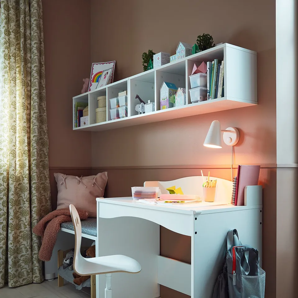 A white kids desk, SMÅGÖRA, with a chair and shelves, featuring a lamp, books, toys, and a bed. Efficient, playful, and organised childrens room.