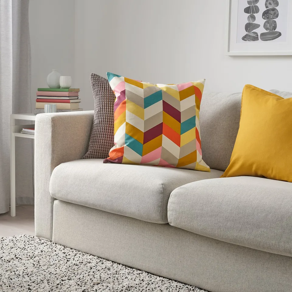 Modern living room with grey sofa, colourful chevron-patterned HANNELISE pillow, yellow pillow, and stacked books on a side table.
