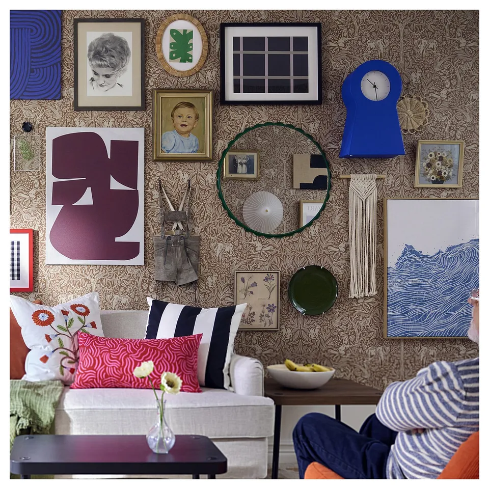 Colourful wall with framed pictures, blue clock, green mirror, sofa with striped and floral pillows.